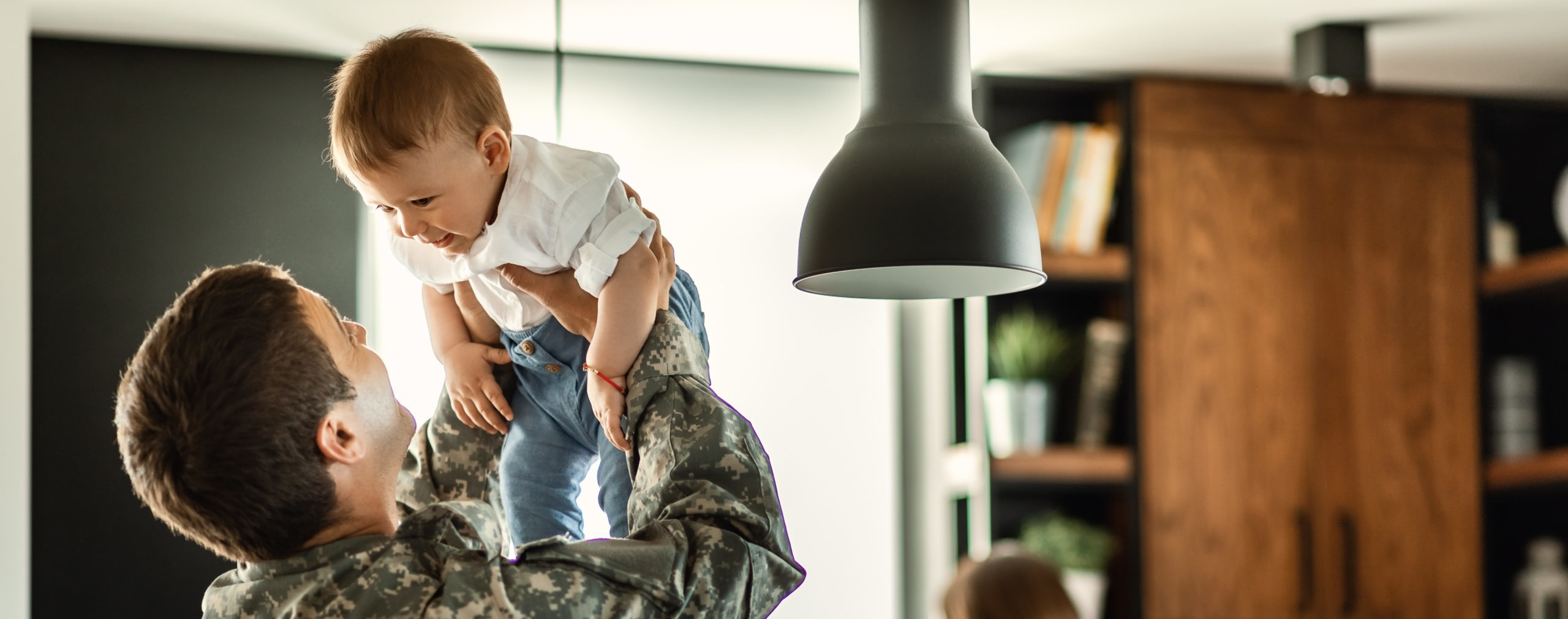 Man wearing army clothing holding up young son at home