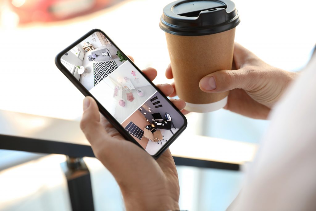 smart home user on phone monitoring house with coffee in other hand.